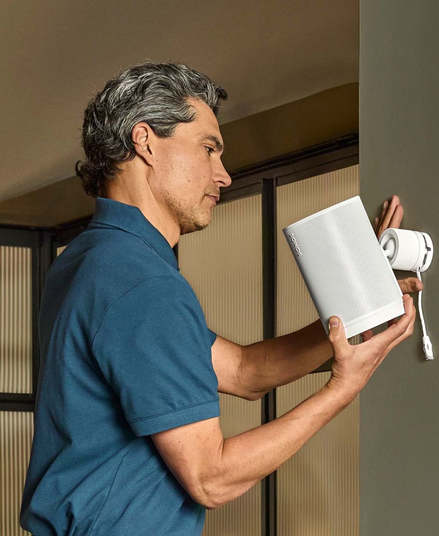 Man in blue polo shirt servicing a white sonos wall-mounted speaker